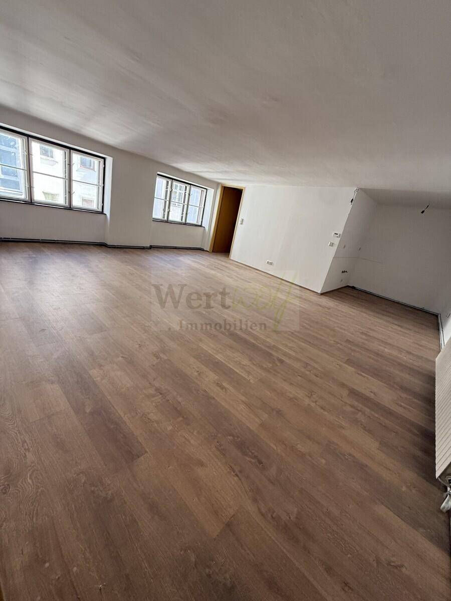 Geräumiger Dachbodenraum mit schrägen Wänden, Laminatboden und mehreren Fenstern.