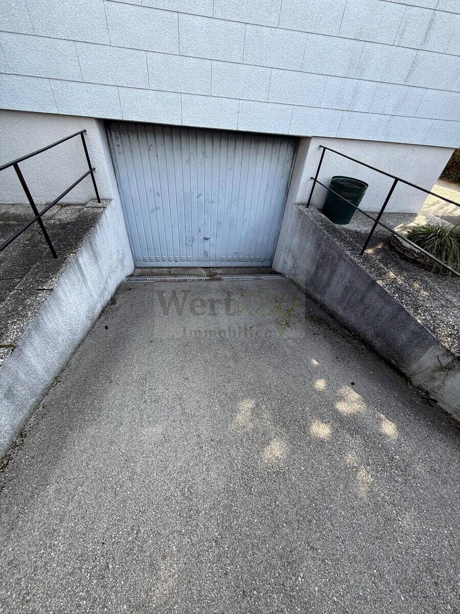 Zufahrt zur Tiefgarage mit Betonrampe und einem einfachen Garagentor.