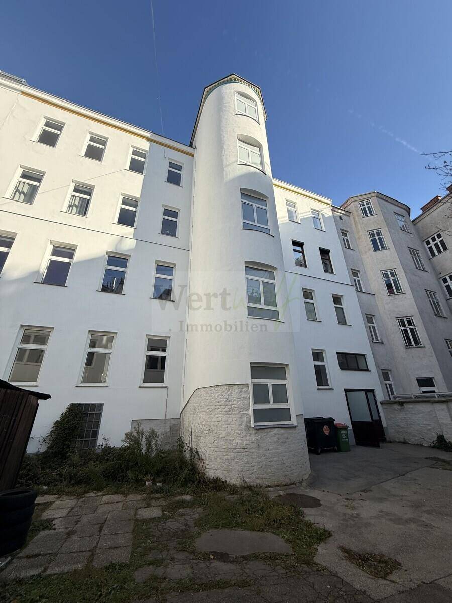 Rückansicht des Gebäudes mit einem runden Turm und einem Innenhofbereich unter blauem Himmel.