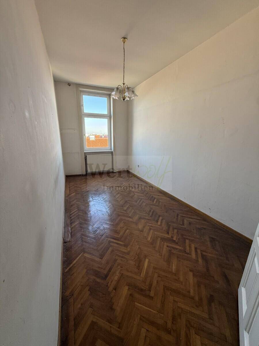 Langes, helles Zimmer mit Fischgrätparkett und einem Fenster, das viel Tageslicht hereinlässt.