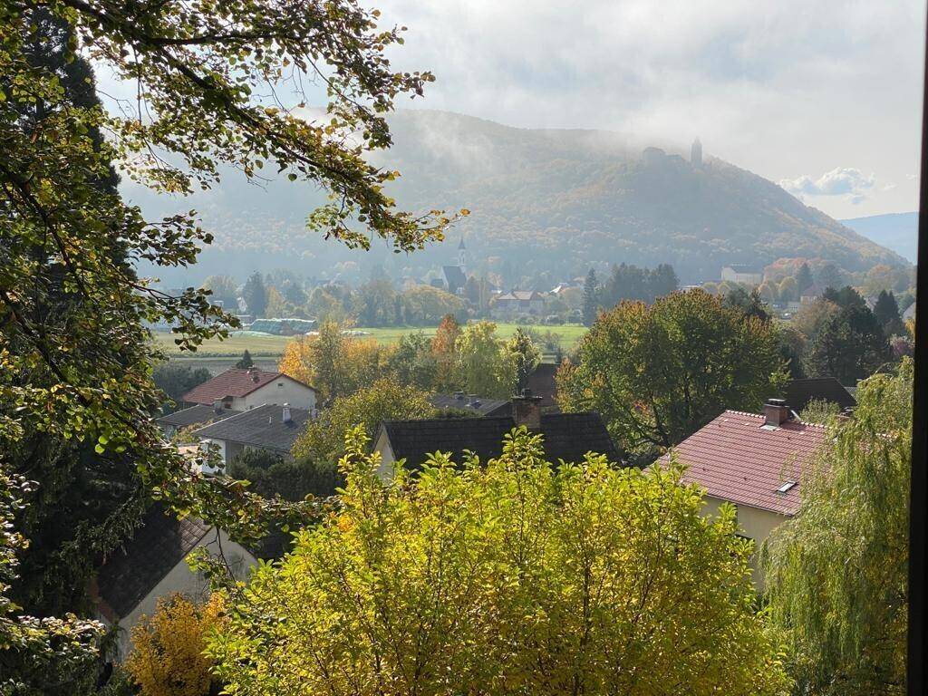 Weitblick aus dem Fenster über eine grüne Hügellandschaft mit Häusern und Bergen.