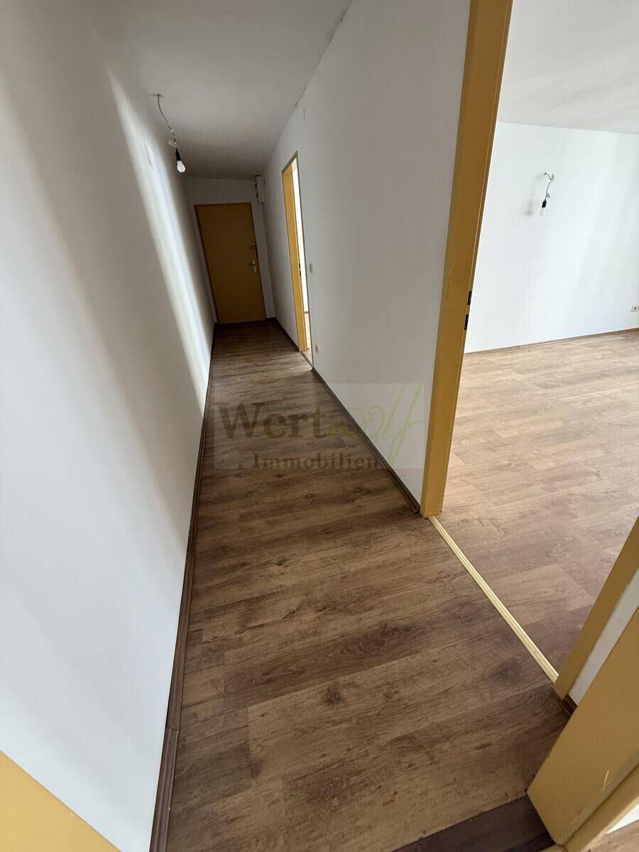Heller Flur mit Laminatboden und weißen Wänden, der zu weiteren Räumen führt.