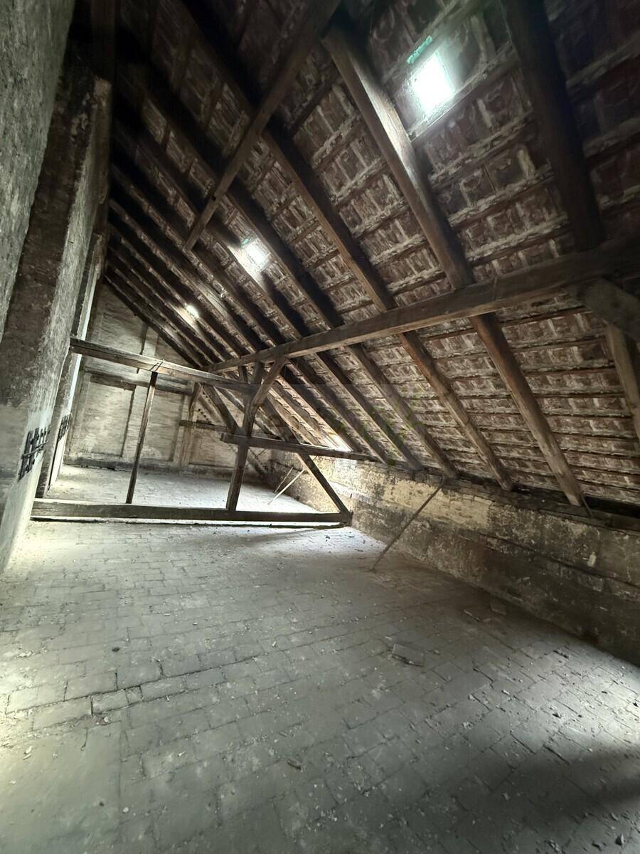 Geräumiger, unausgebauter Dachboden mit sichtbaren Holzbalken und Ziegelboden.