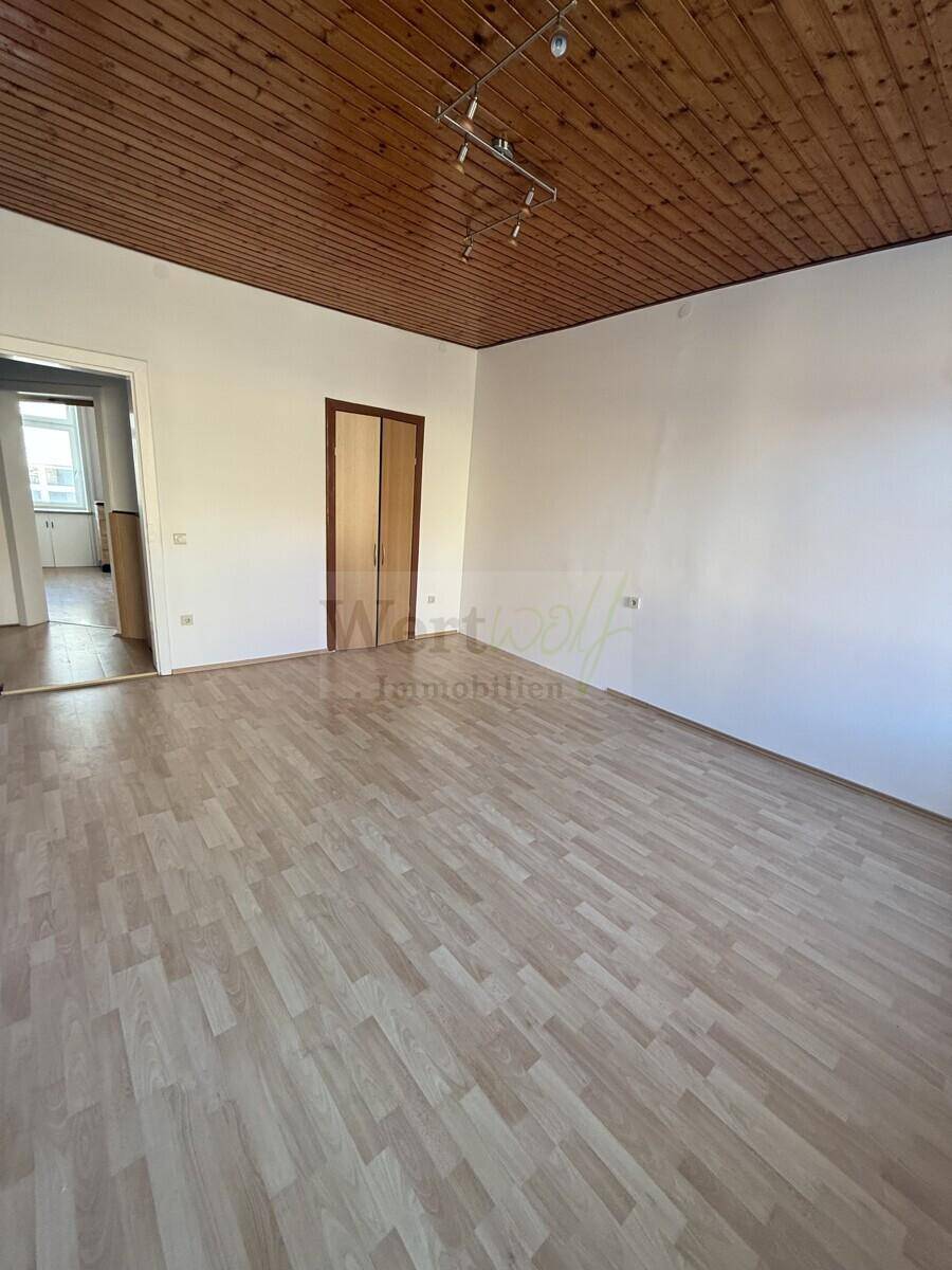 Helles Zimmer mit Parkettboden und Holzdecke, das einen Zugang zu einem angrenzenden Bereich bietet.