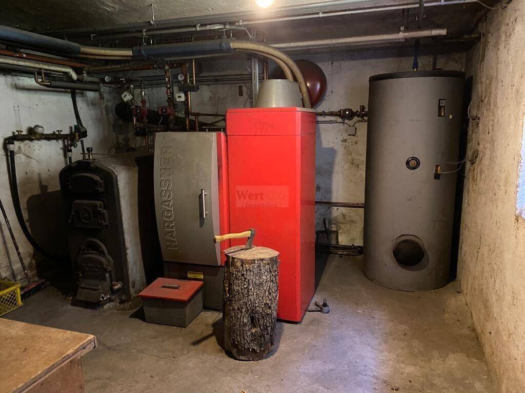 Heizungsraum im Keller mit großem Holzkessel, Warmwasserspeicher und Rohren.