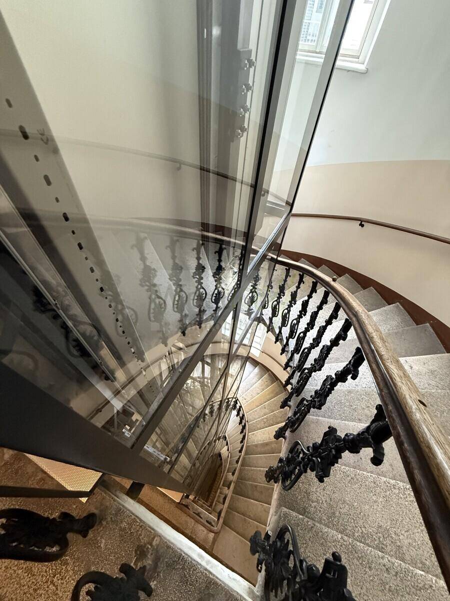 Blick von oben auf eine historische Wendeltreppe mit schmiedeeisernem Geländer und Glasaufzug.