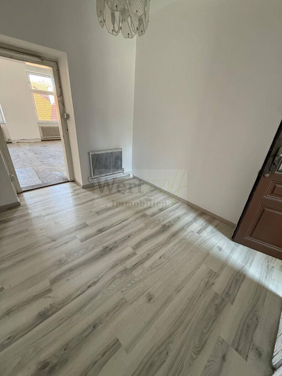 Raum mit hellem Laminatboden und einem Heizkörper unter dem Fenster, der auf eine Renovierung wartet.