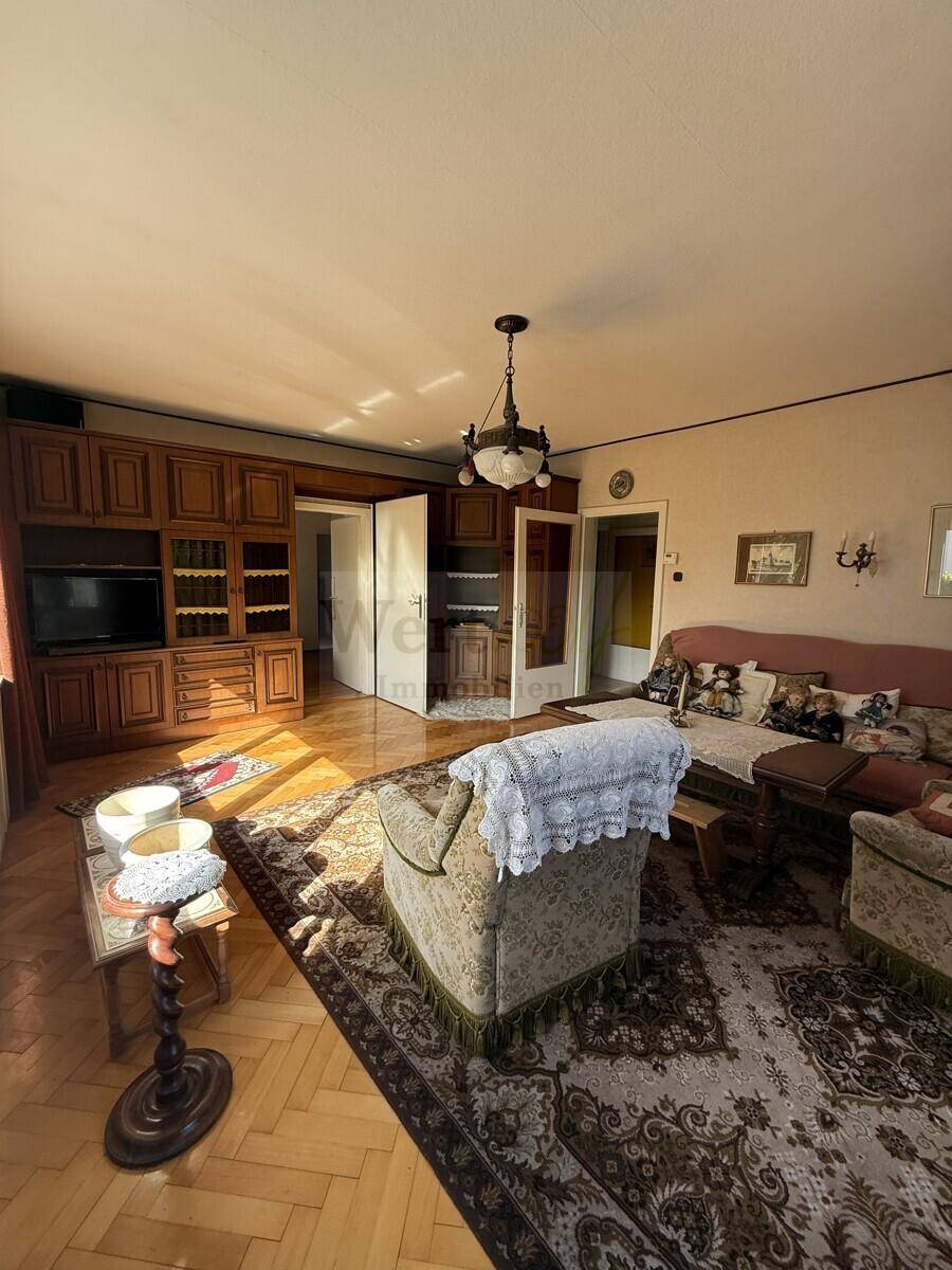 Helles Wohnzimmer mit Parkettboden, bequemen Sitzgelegenheiten und einem großen Holzschrank.