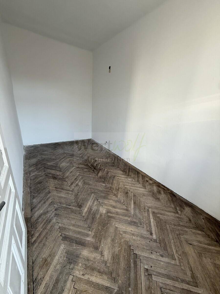 Kleineres Zimmer mit dunklem Fischgrätparkettboden und einem Fenster, das auf einen Innenhof blickt.