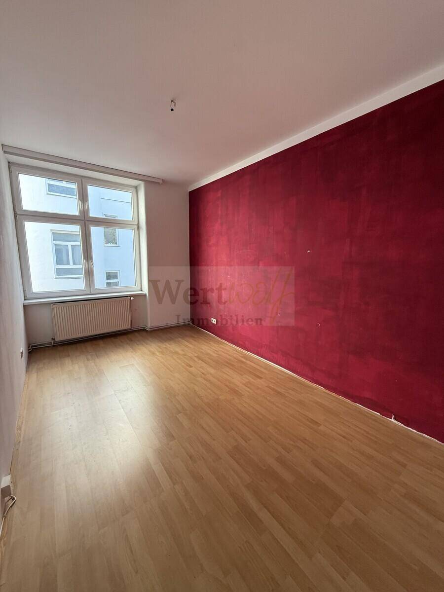 Schlafzimmer mit Laminatboden und einer auffälligen roten Akzentwand.