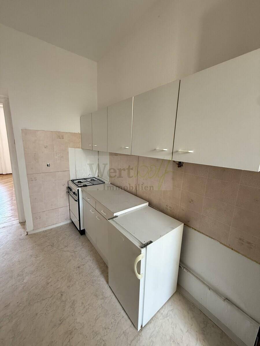 Küche mit weißen Oberschränken, Gasherd und Kühlschrank, renovierungsbedürftig.