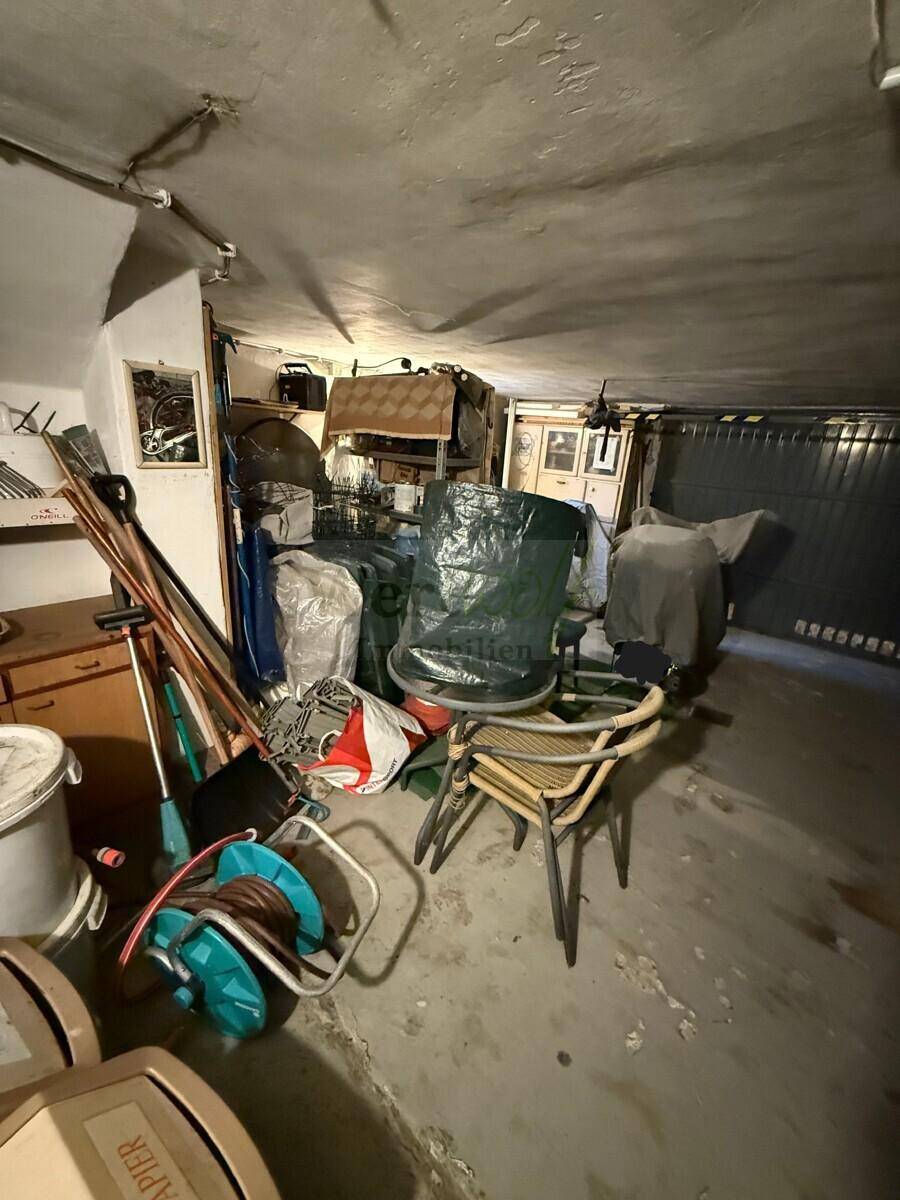 Unaufgeräumter Garagenraum mit Betonboden, der als Abstellfläche für diverse Gegenstände dient.