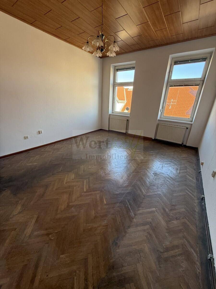 Heller Raum mit Fischgrätparkett, Holzdecke und Blick auf die umliegenden Dächer und Gebäude.