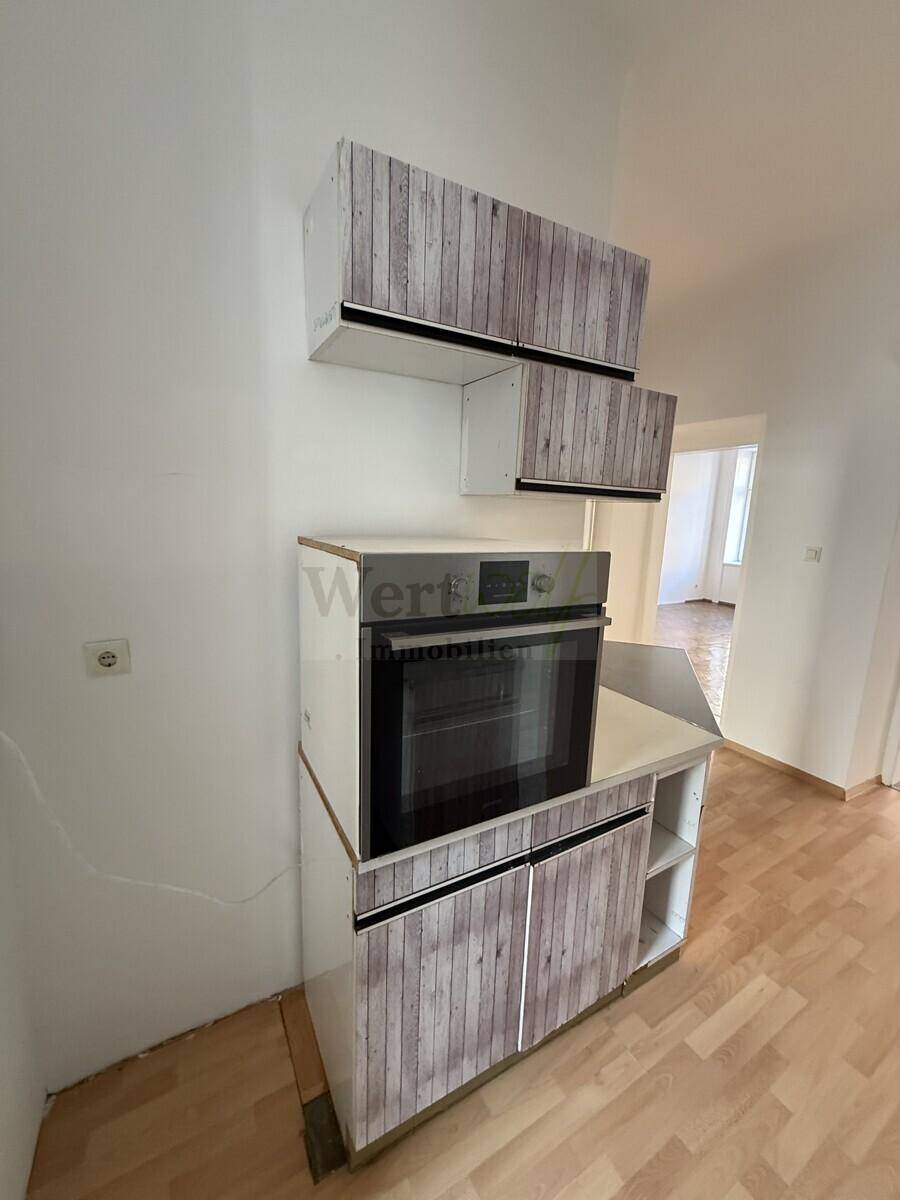 Küchenbereich mit Einbauofen und Schränken in heller Holzoptik, die eine Auffrischung benötigen.