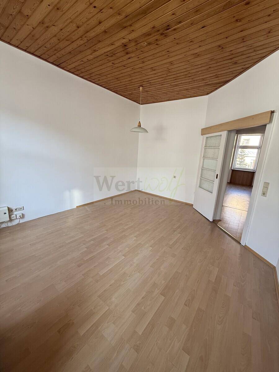 Geräumiges Zimmer mit Parkettboden und Holzdecke, das durch eine Schiebetür mit einem weiteren Raum verbunden ist.