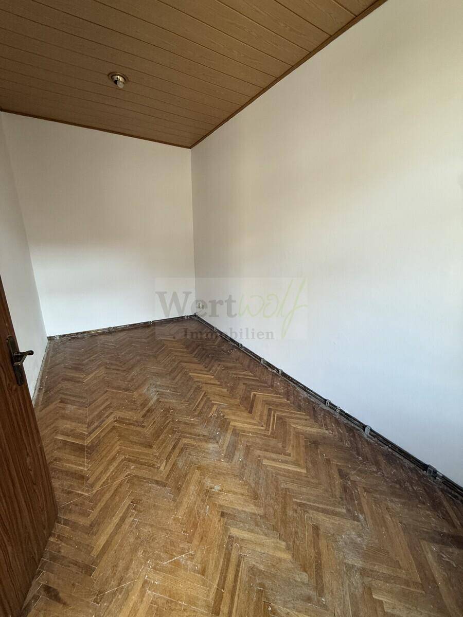 Detailansicht des abgenutzten Fischgrätparketts und der Holzdecke in einem leeren Raum.