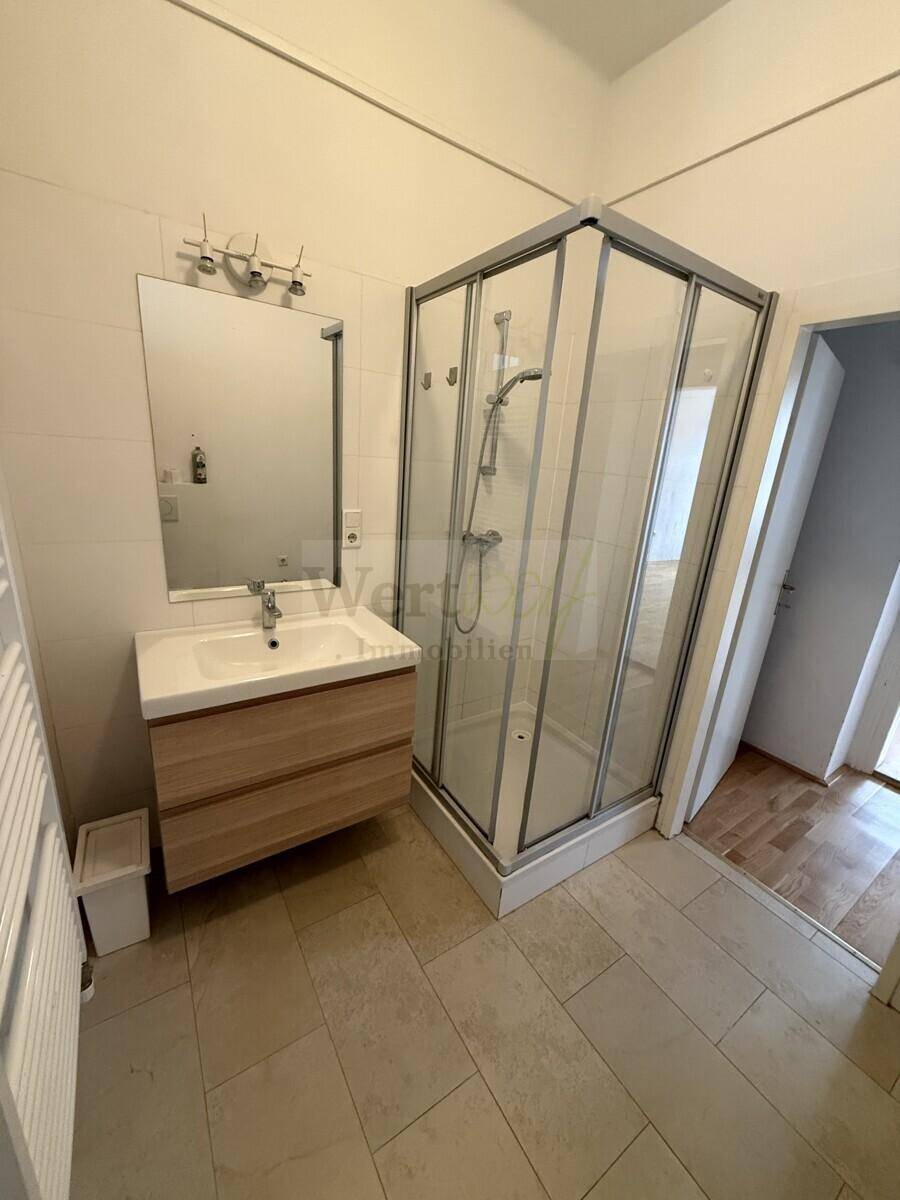 Badezimmer mit Duschkabine, modernem Waschtisch und großem Spiegel, funktional und hell.