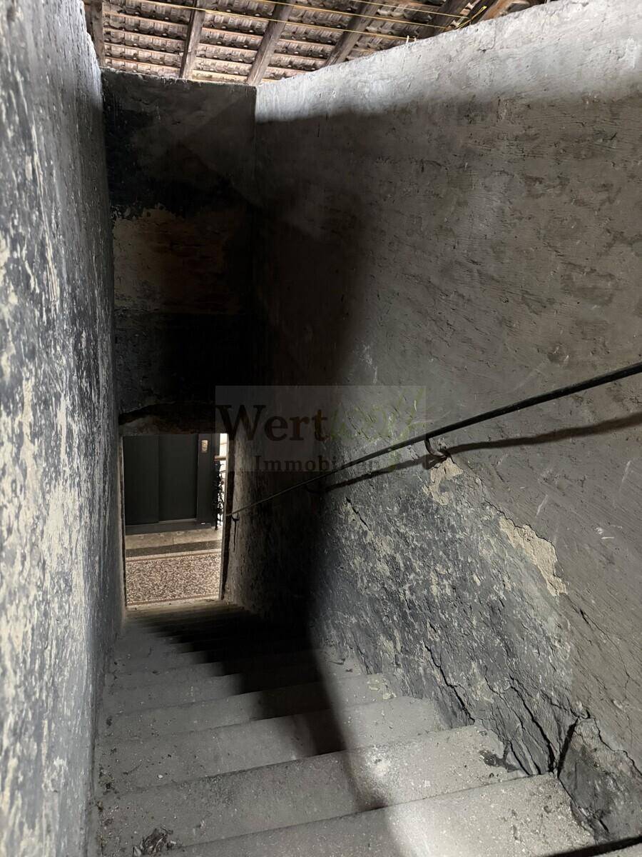 Schmale Treppe führt vom Dachboden hinunter, umgeben von rauen Wänden.