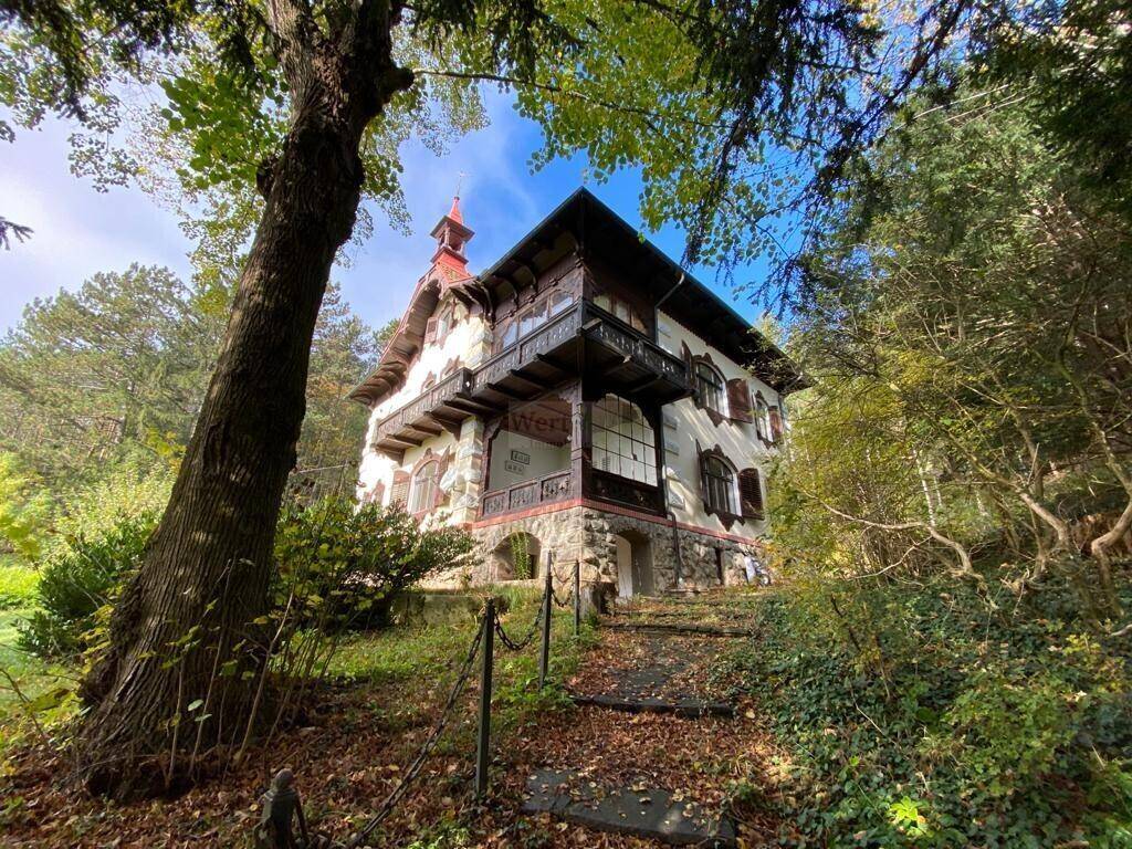 Historisches Anwesen mit Steinmauern und Holzelementen, umgeben von üppiger Vegetation und alten Bäumen.