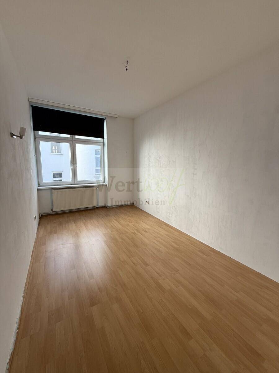 Geräumiges Schlafzimmer mit Laminatboden und Rollladen am Fenster.