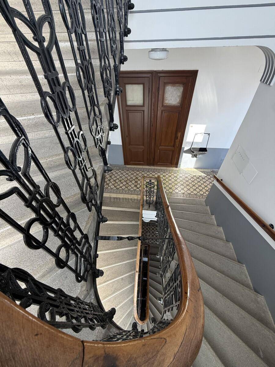 Blick von oben auf das historische Treppenhaus mit kunstvollem schmiedeeisernem Geländer und gemusterten Fliesen.