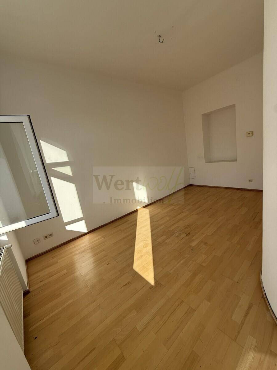 Helles Zimmer mit Holzparkett und einem Fenster, das viel Sonnenlicht in den Raum bringt.