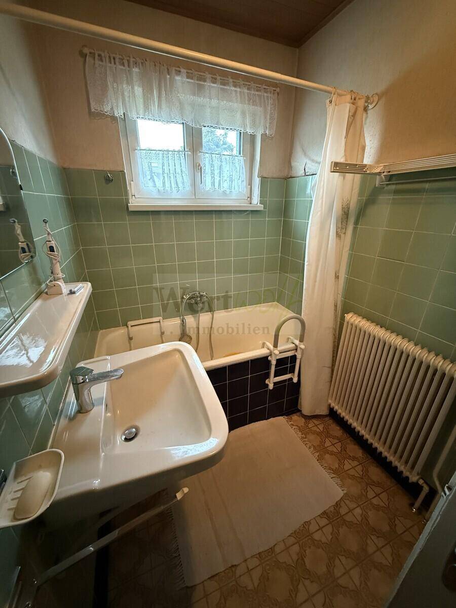 Badezimmer mit grünen Wandfliesen, Badewanne, Waschbecken und Fenster.