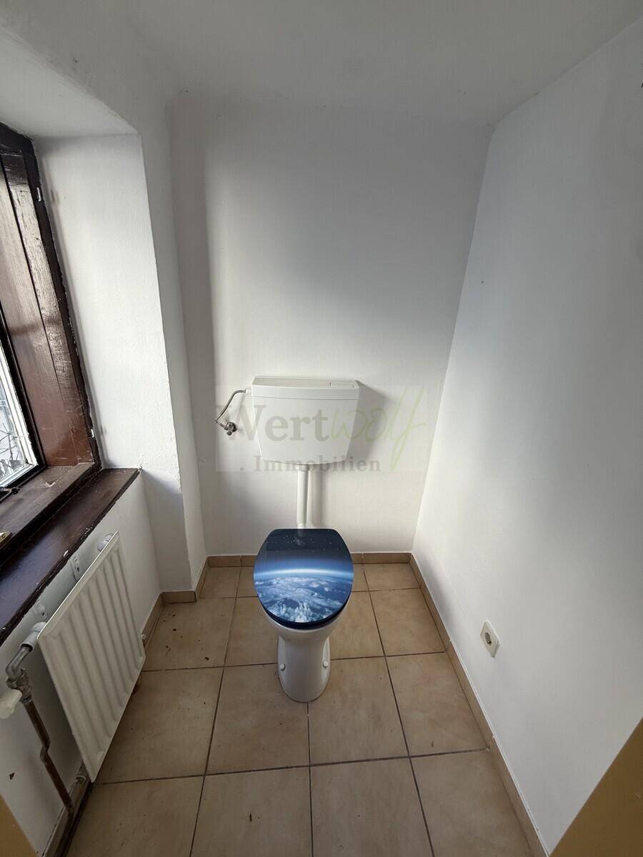 Separate Toilette mit Fenster, Fliesenboden und einem Heizkörper.