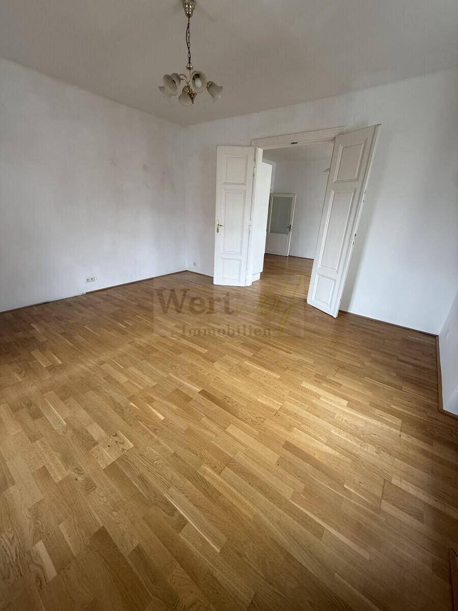 Leeres Zimmer mit Parkettboden und Flügeltüren, die zu einem angrenzenden Raum führen.