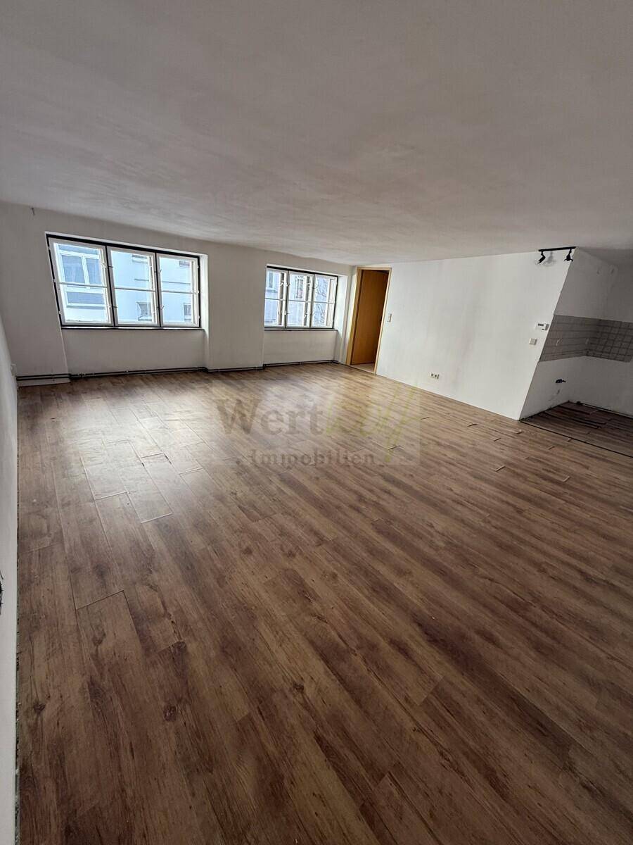 Offener Wohnbereich mit Laminatboden und vorbereiteter Ecke für eine Küchenzeile.