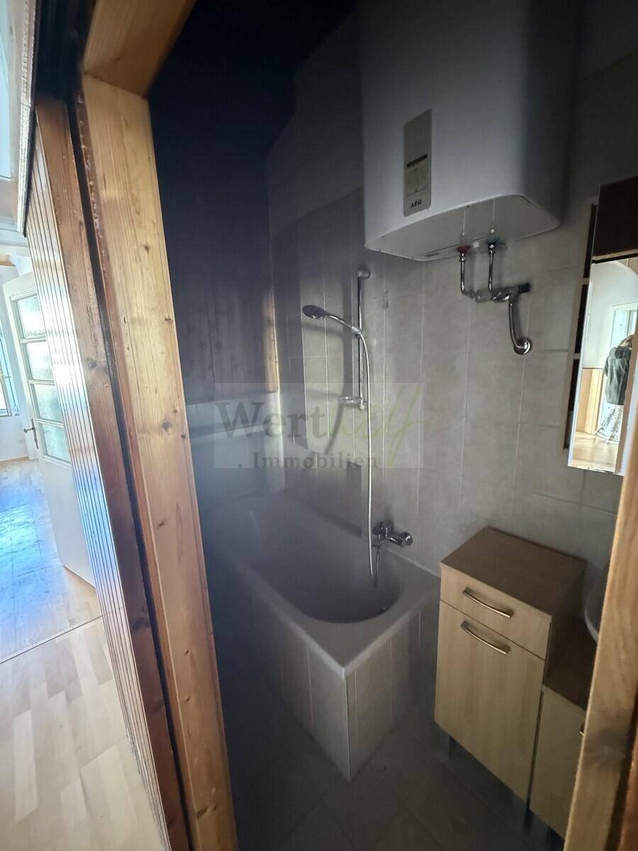 Badezimmer mit Badewanne, Duscharmatur und Fliesen an Wänden und Boden, bietet grundlegenden Komfort.