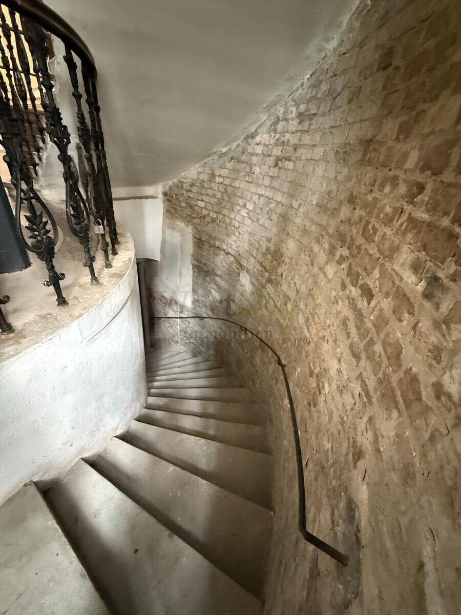 Enge Wendeltreppe mit unverputzter Ziegelwand und schmiedeeisernem Geländer.