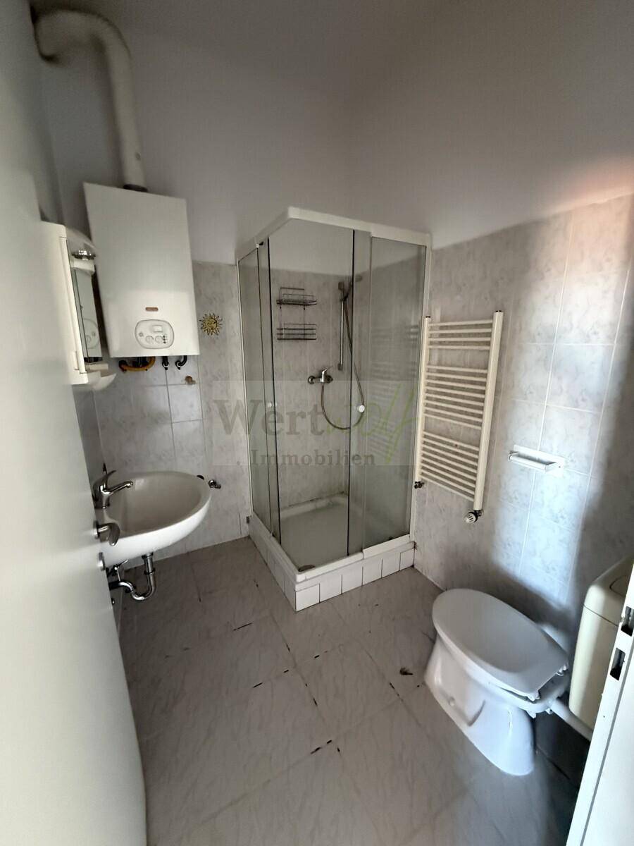 Badezimmer mit Duschkabine, Waschbecken, Toilette und Heizkörper, alles in hellem Design.