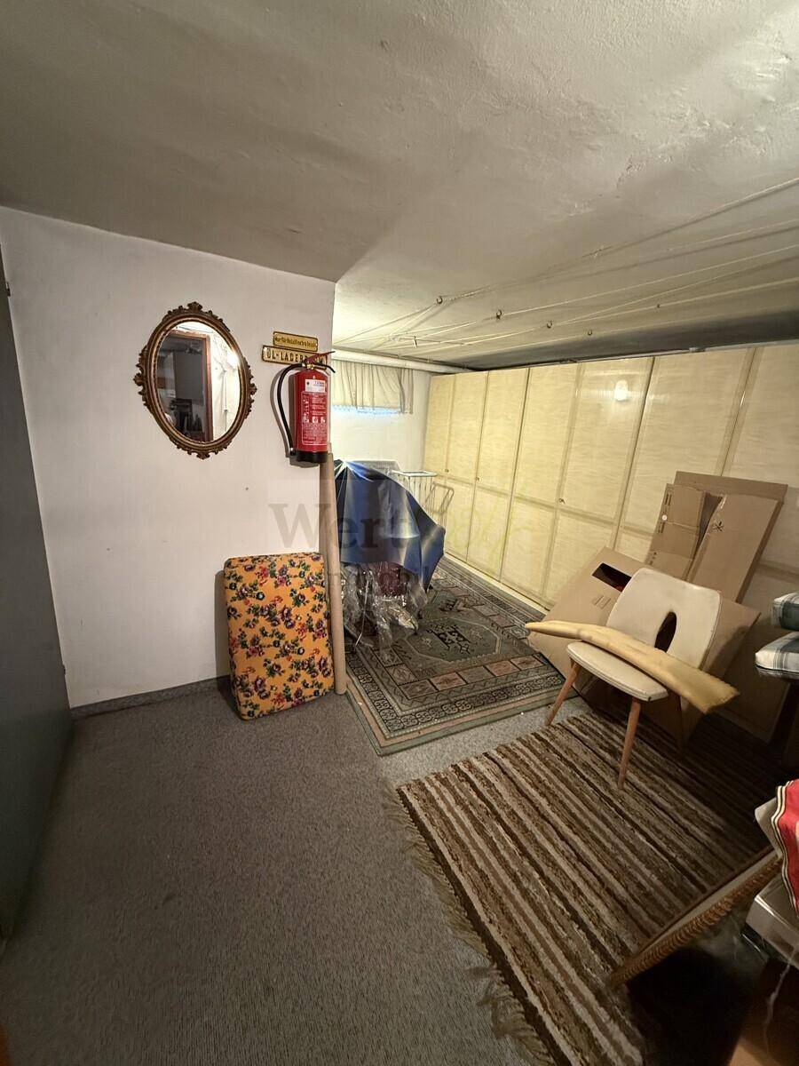 Kellerraum mit Teppichboden, Spiegel und verschiedenen gelagerten Gegenständen.
