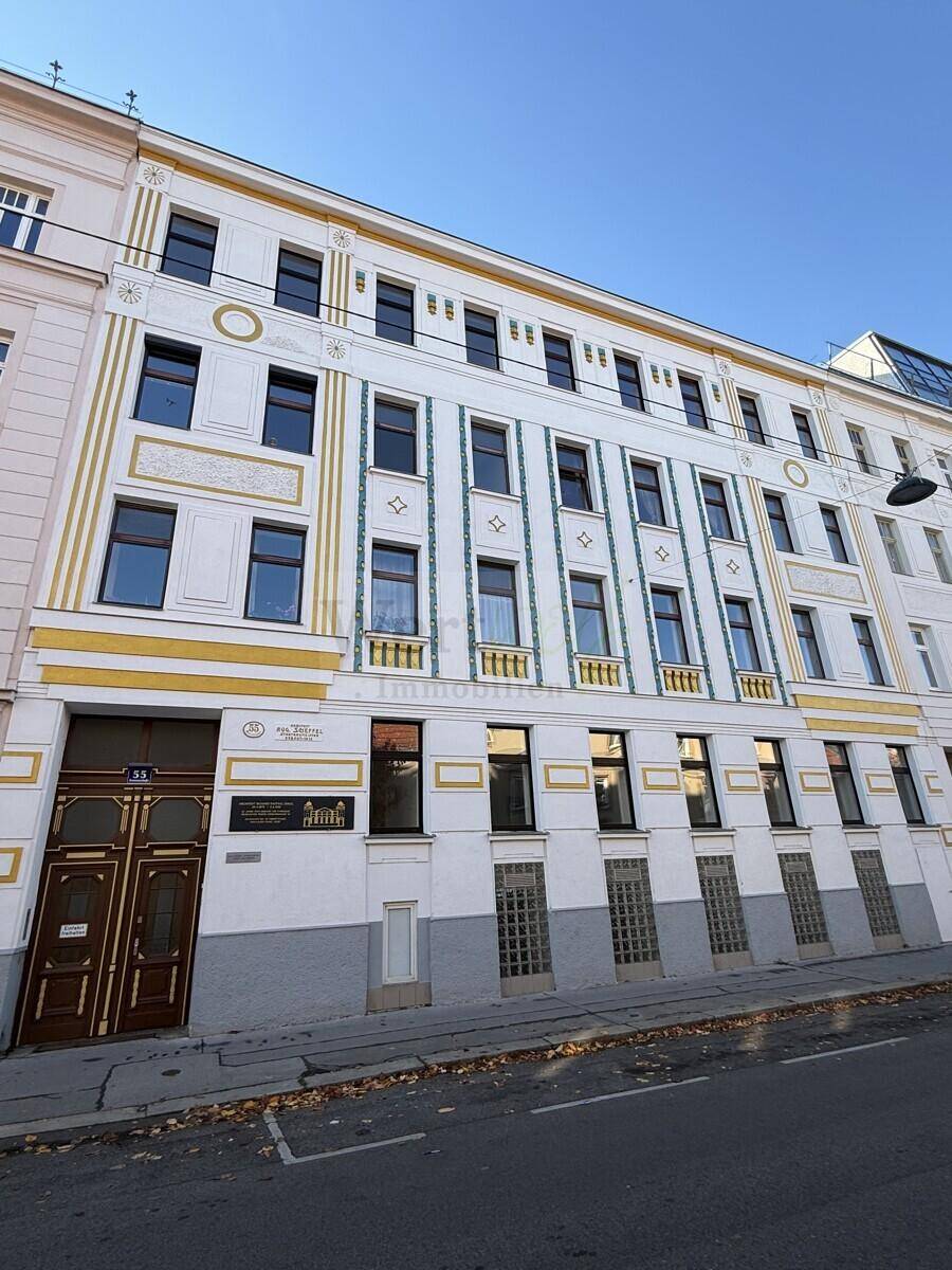 Historische Fassade eines Mehrfamilienhauses mit dekorativen Elementen und großen Fenstern zur Straße hin.