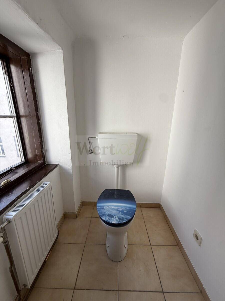 Kleines WC mit Fenster, Heizkörper und gefliestem Boden, ausgestattet mit einer Toilette.