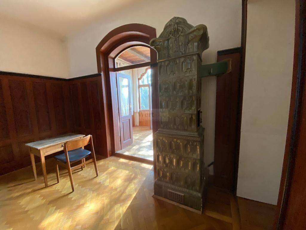 Heller Raum mit Fischgrätparkett, Holzvertäfelung und einem traditionellen Kachelofen.