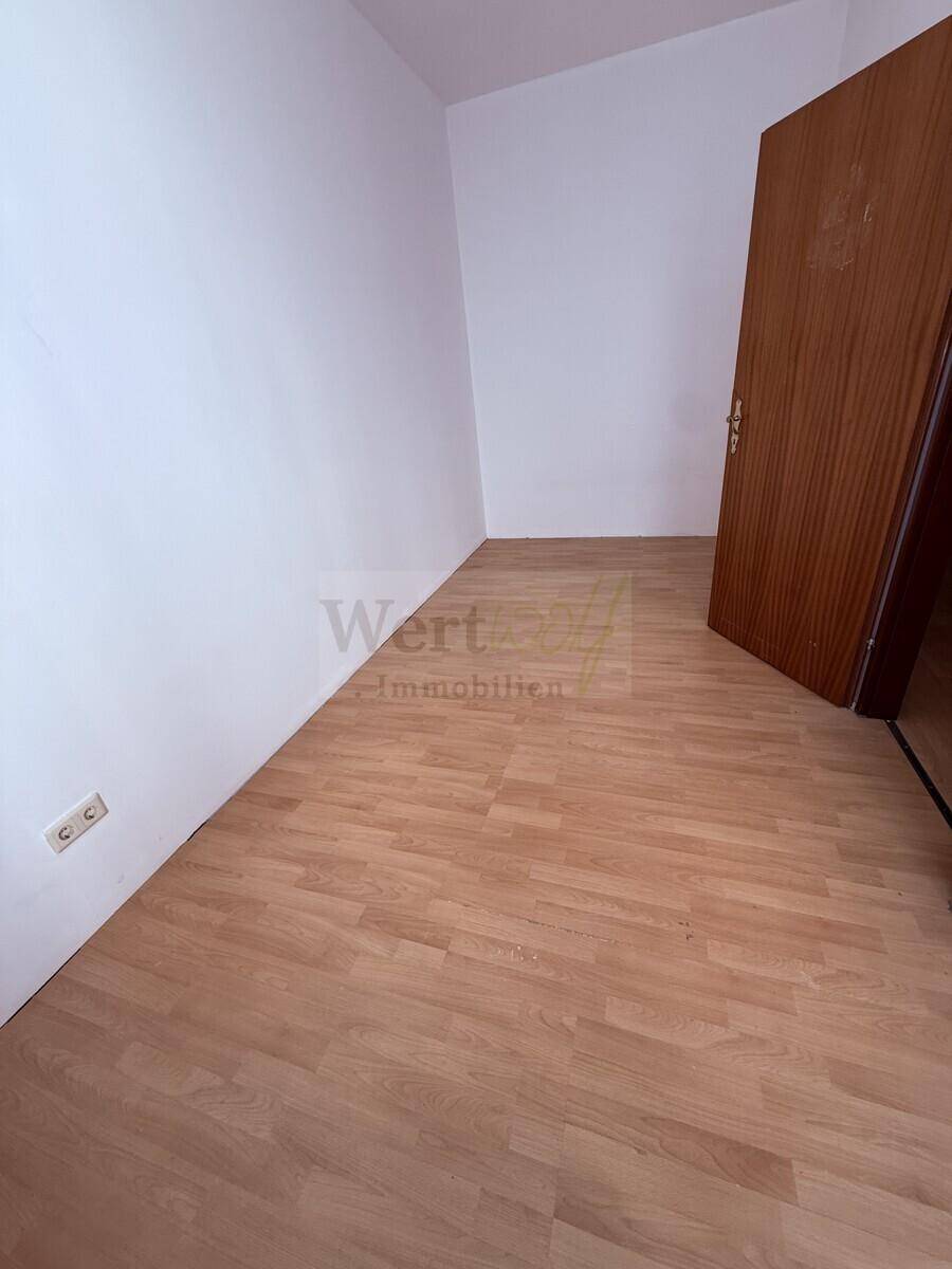 Eckansicht eines leeren Zimmers mit Laminatboden und einer Holztür.