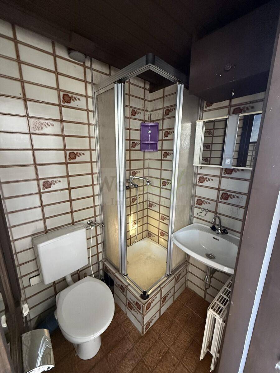 Kompaktes Badezimmer mit Duschkabine, WC und Waschbecken, ausgestattet mit braunen Fliesen.