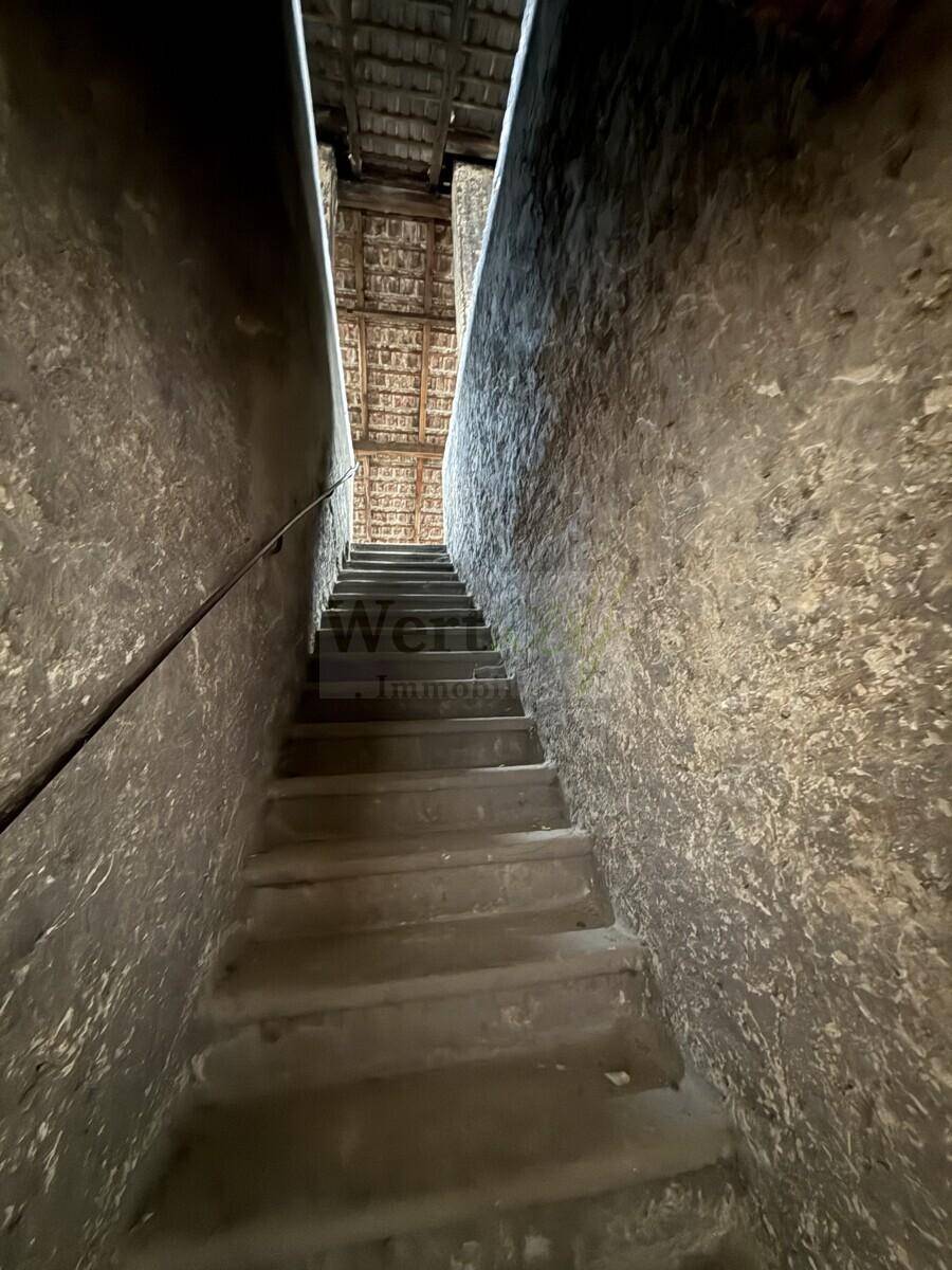 Dunkle, schmale Treppe führt hinauf zum Dachboden mit sichtbarer Holzkonstruktion.