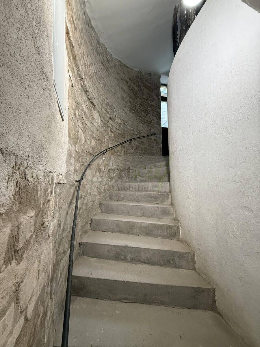 Steile Wendeltreppe mit rauer Ziegelwand und schlichtem Handlauf.