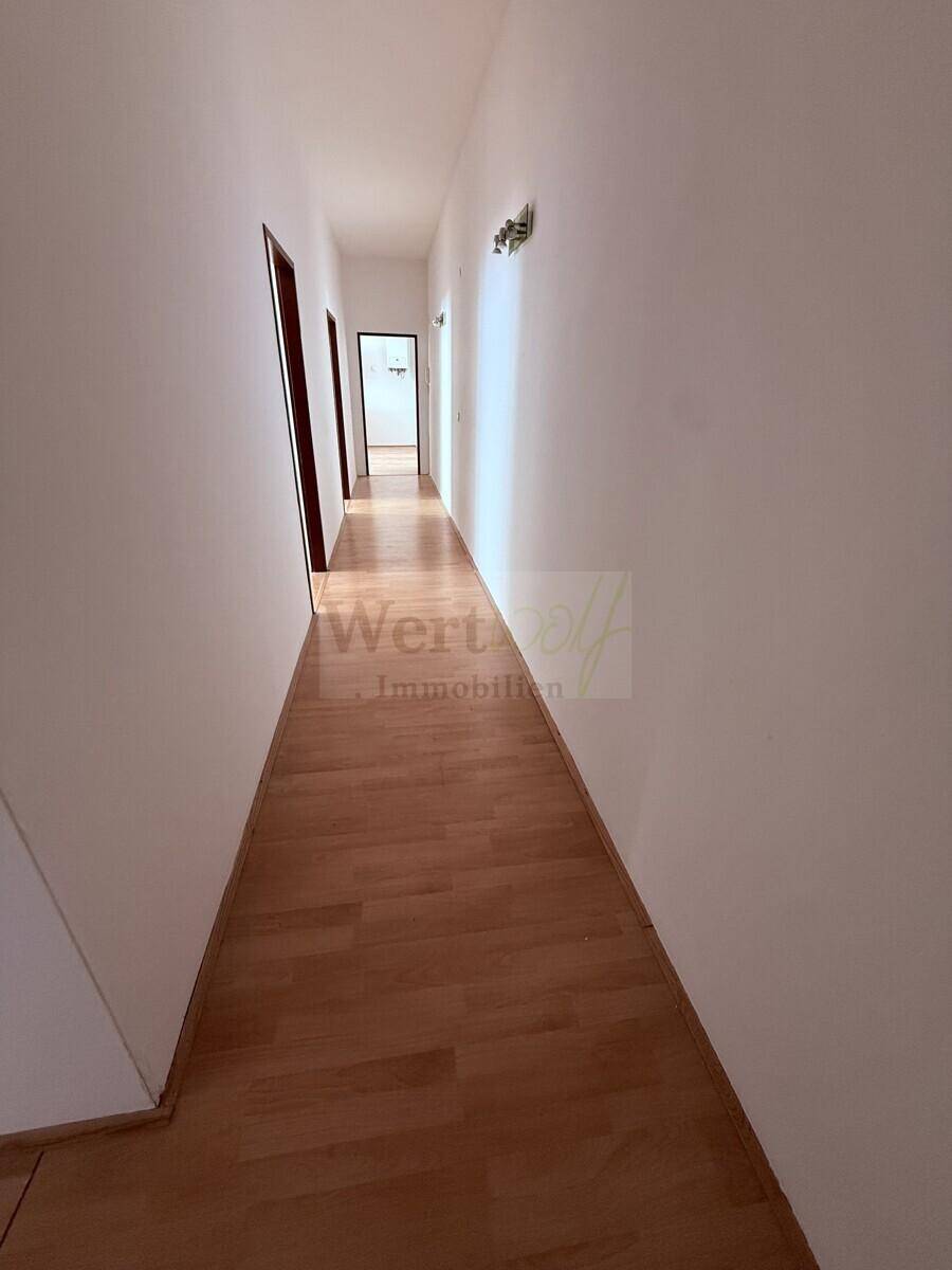 Langer, schmaler Flur mit hellem Laminatboden und mehreren Türen zu den Zimmern.
