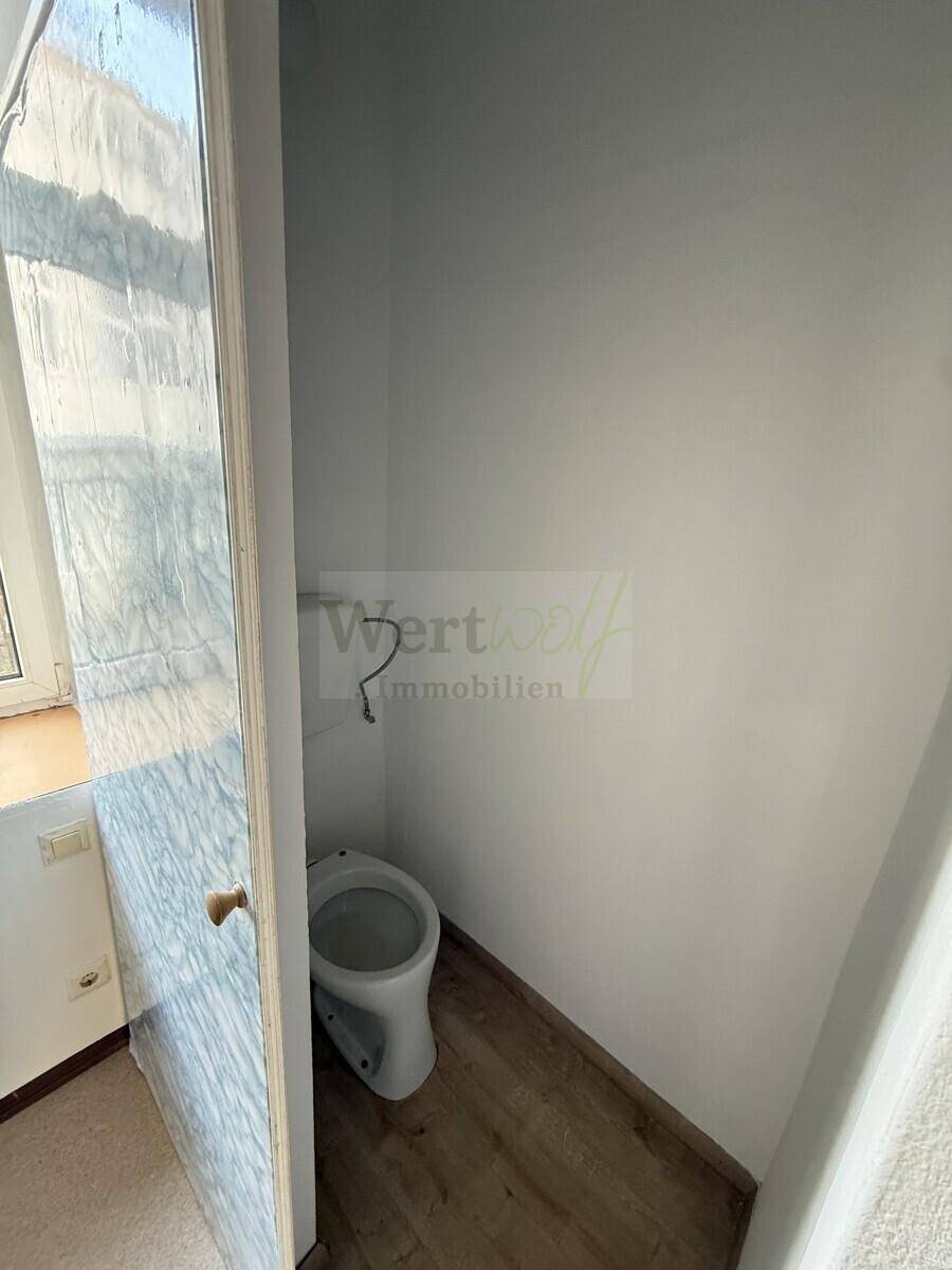 Separates WC mit einfacher Toilette und Laminatboden, das eine Modernisierung erfordert.