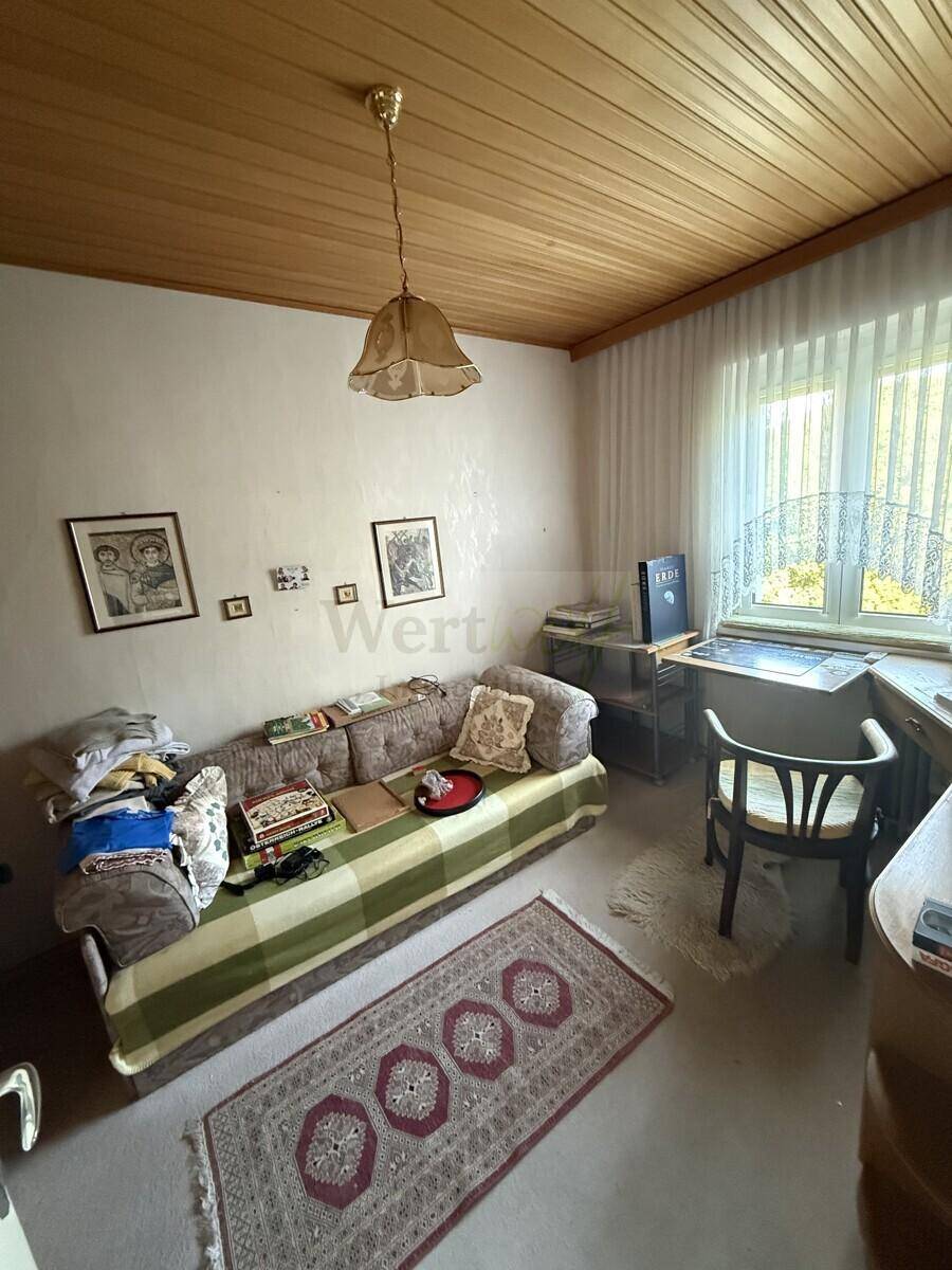Helles Wohnzimmer mit Sofa, Schreibtisch und einer warmen Holzdecke, ideal zum Entspannen.