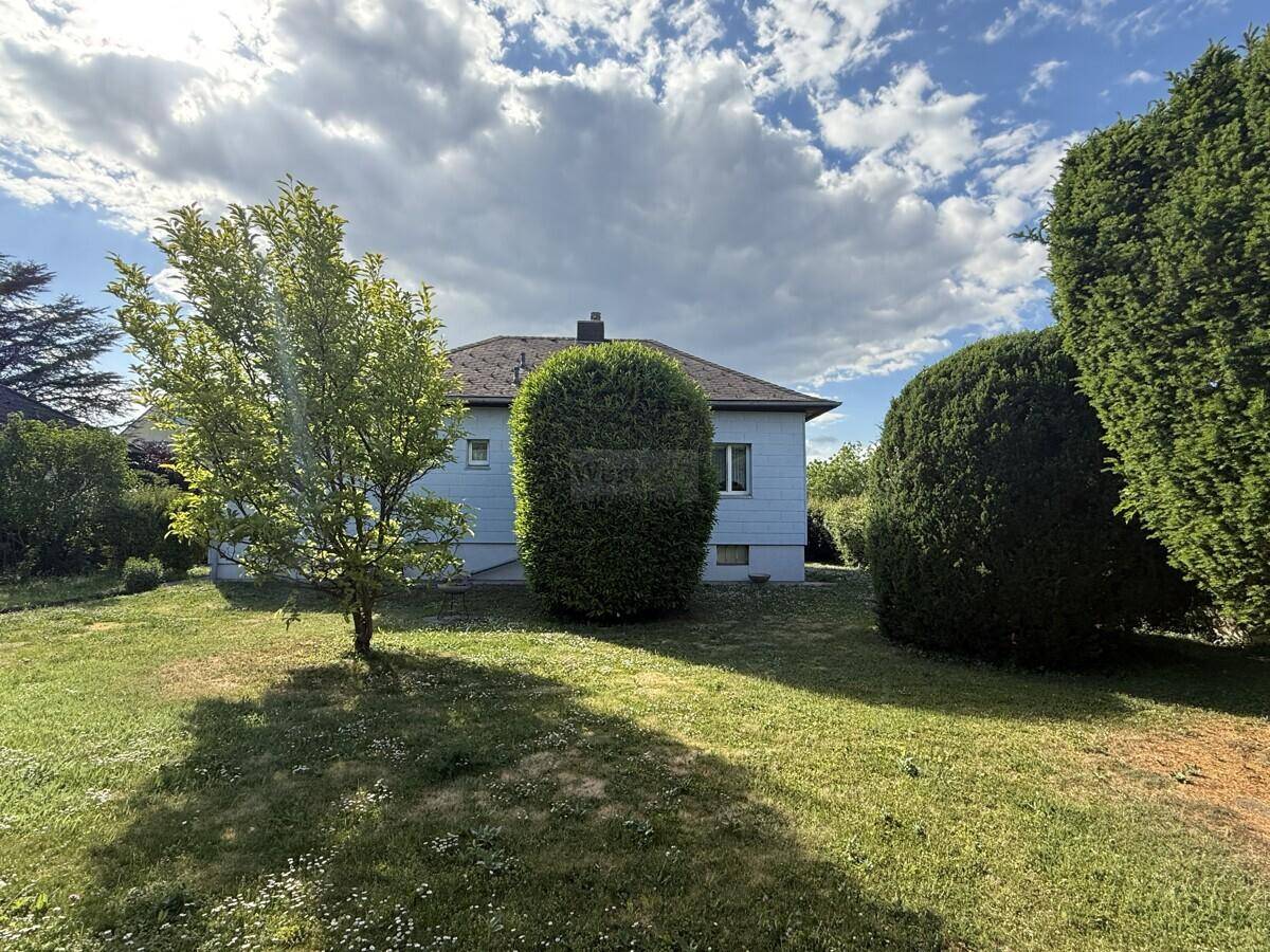 Rückansicht des Hauses vom weitläufigen Garten aus, umgeben von hohen Bäumen und Grünflächen.