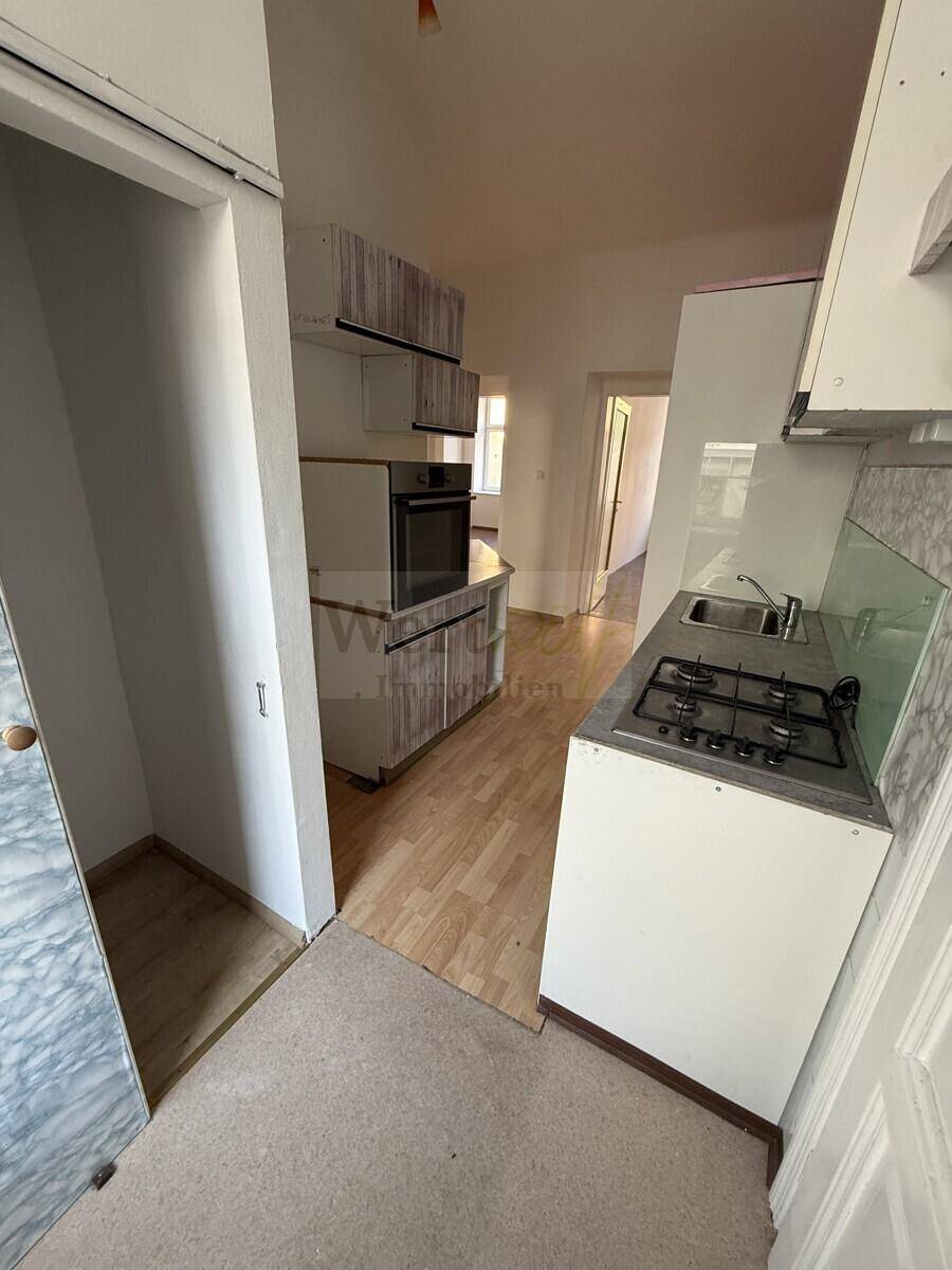 Kleine Küche mit einfacher Ausstattung, Gasherd und Laminatboden, die eine Renovierung benötigt.