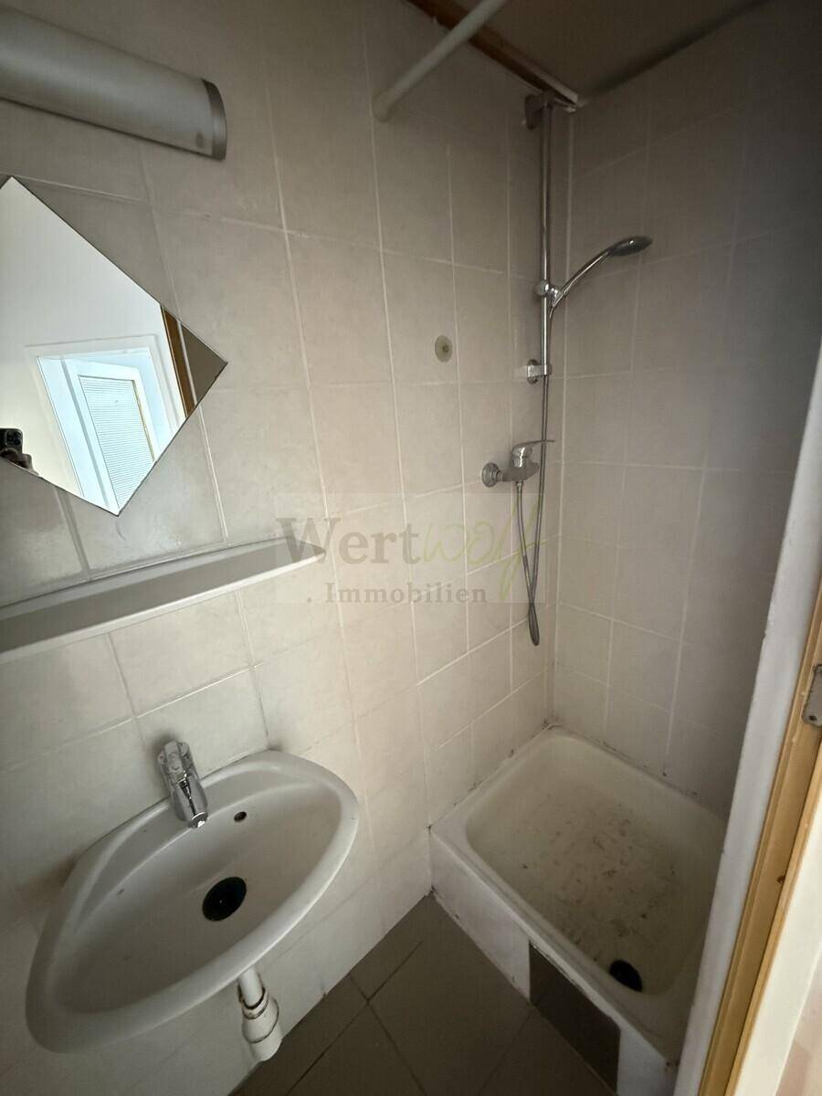 Kleines Badezimmer mit Dusche, Waschbecken und weißen Fliesen im Stil der 80er Jahre.