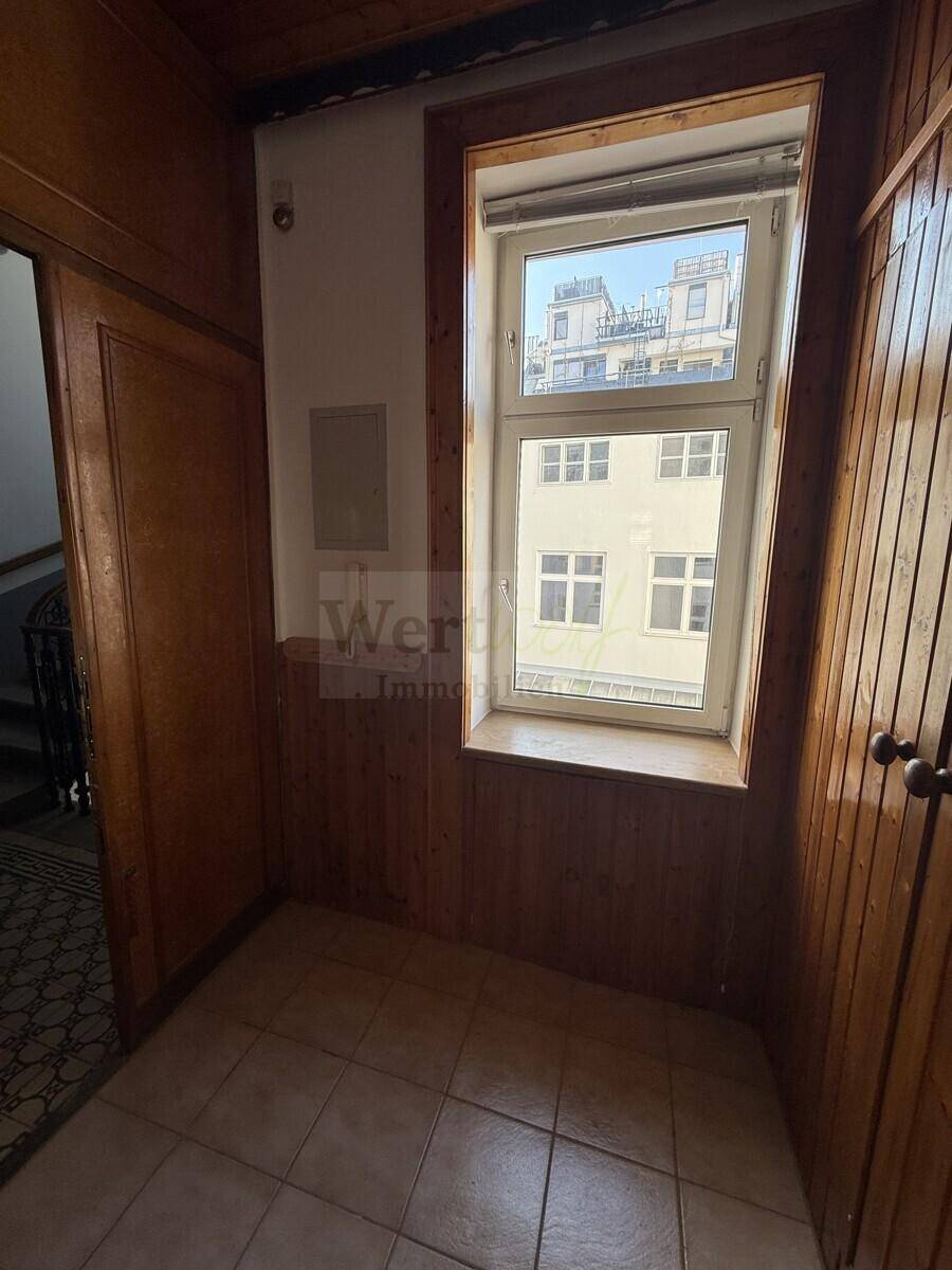 Heller Bereich im Flur mit Holzvertäfelung, Fliesenboden und einem Fenster mit Blick nach draußen.