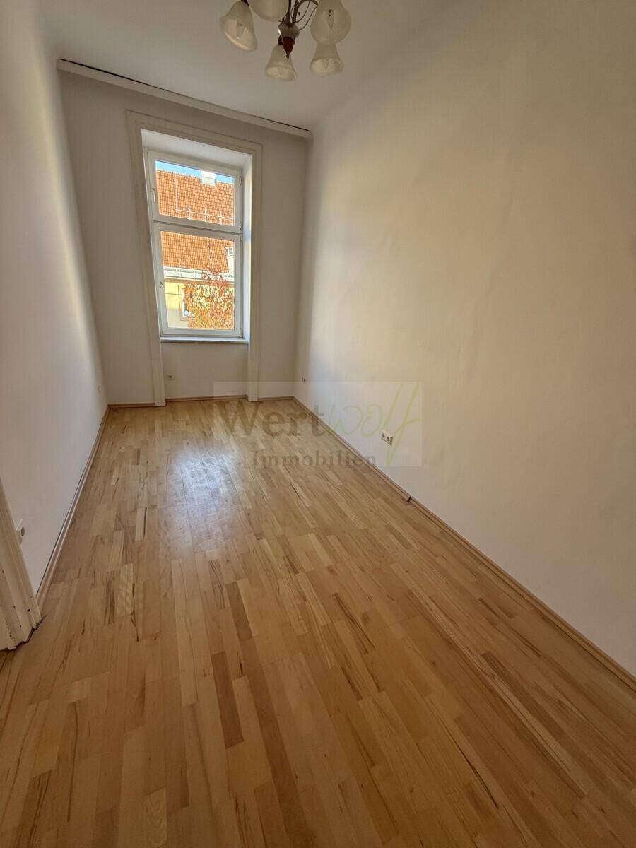 Helles Zimmer mit Parkettboden und einem Fenster, das viel Tageslicht hereinlässt, ideal für Wohnzwecke.