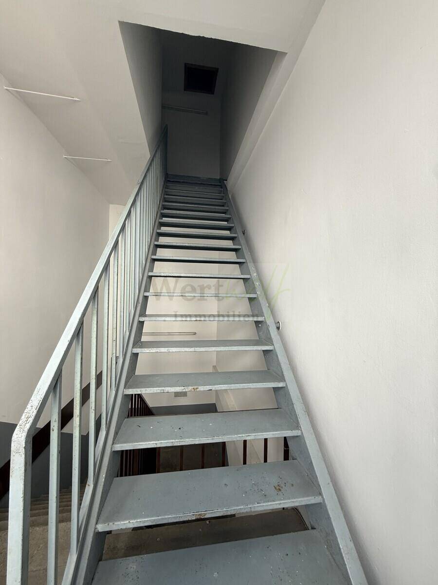 Schlichtes Treppenhaus mit Metallgeländer und weißen Wänden in einem Mehrfamilienhaus.